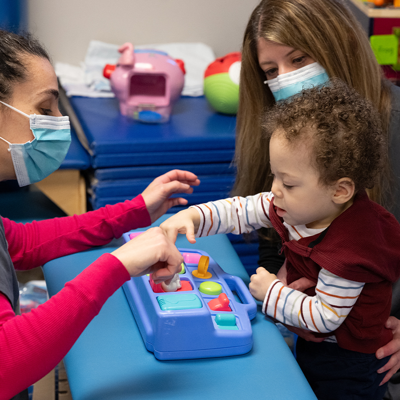 Jace Cruz sitting with two nurses playing with a children's toy