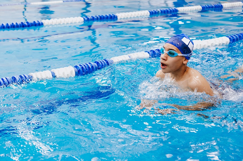 young man teenager swimmer athlete wearing cap and goggles swimming in a pool and training, swimmer's ear