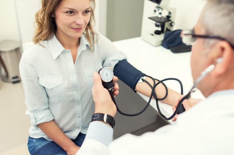 Woman having blood pressure taken by doctor in doctor's office.