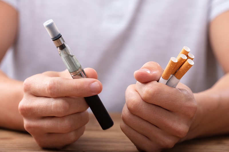Man holding e-cigarette and cigarettes in his hands.