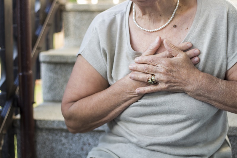 Close up of an elderly woman clutching her chest from chest pain. Heart disease concept. 