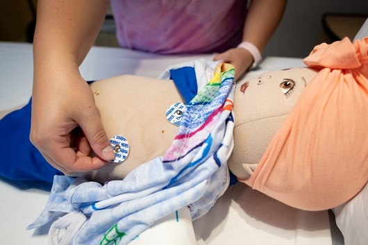 doll getting stickers on their chest for surgery to show pediatric patient