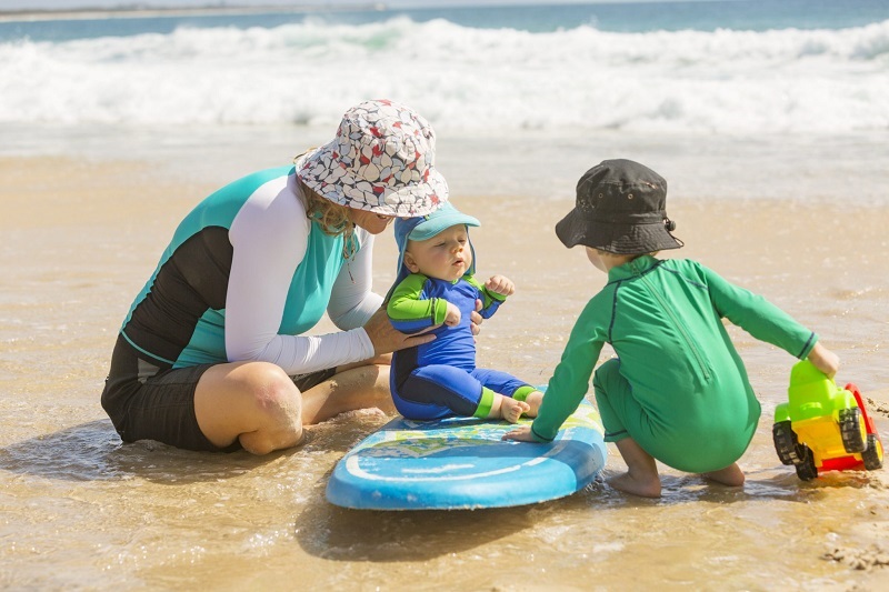 parent and kids playing on beach with sun protective clothes on