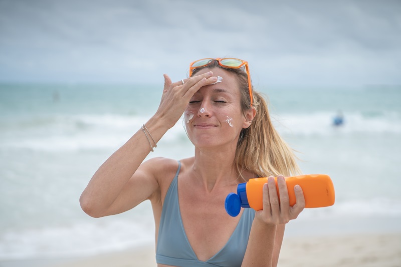 Young woman on beach applying sunscreen on her face, protection on skin and sunbathing tan concept