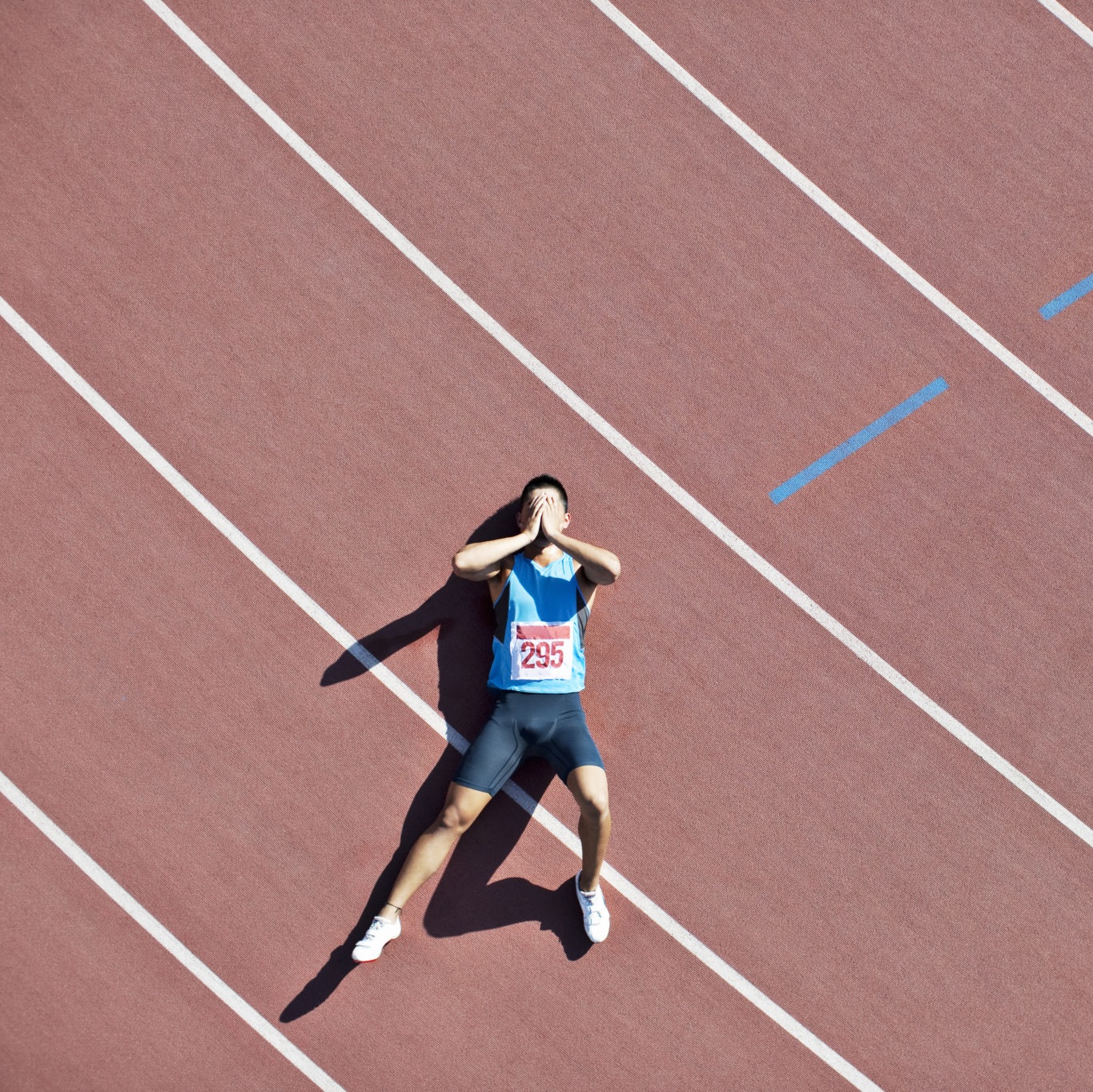 Athlete laying on track covering face with hands
