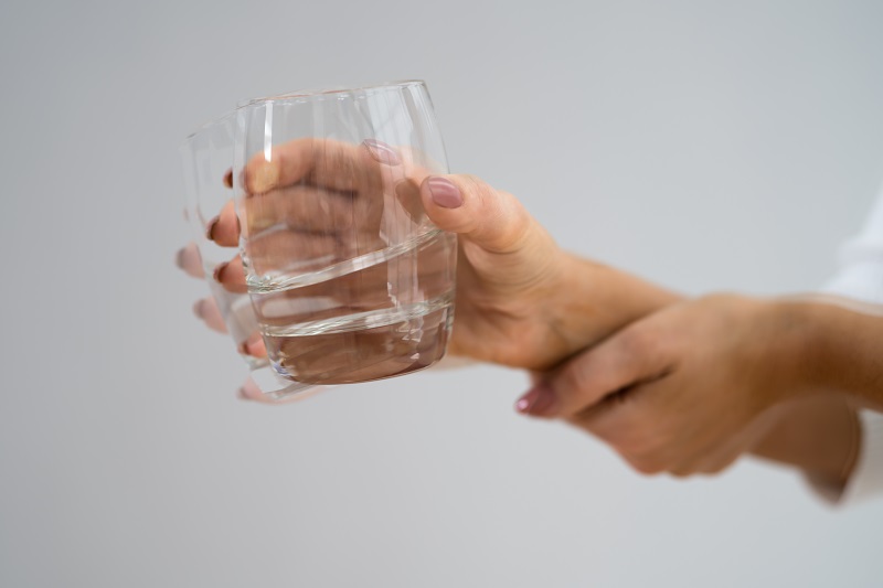 hand shaking from a tremor while holding a glass of water