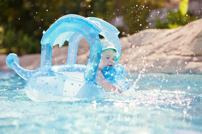 baby sitting in a floating device in a swimming pool splashing 