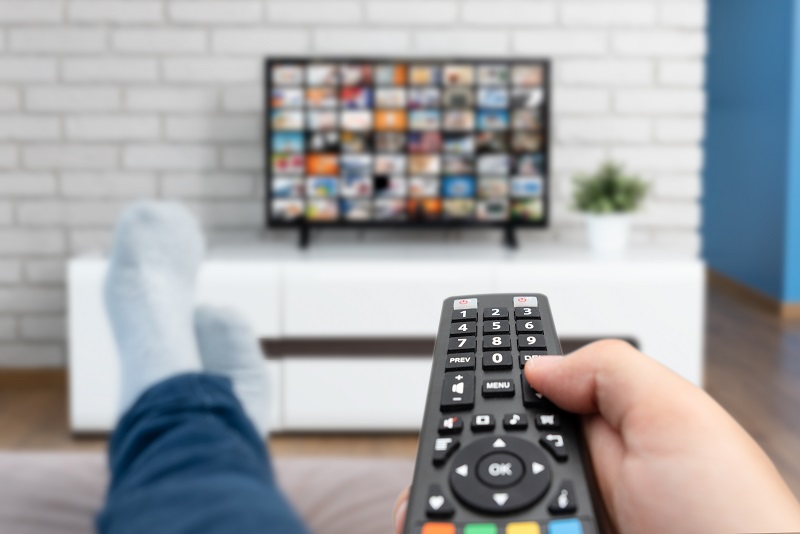 Man laying on sofa, binge watching TV with remote control in his hand.