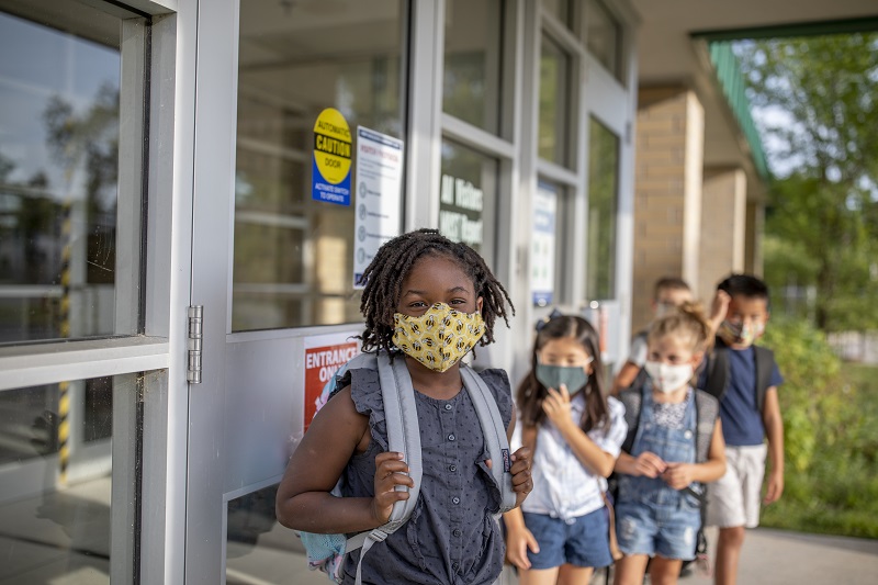 Children waiting in a line outside of their school with masks on. 