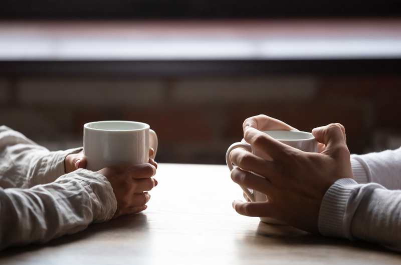 Close up view of a couple holding coffee cups having a serious conversation about STD testing.