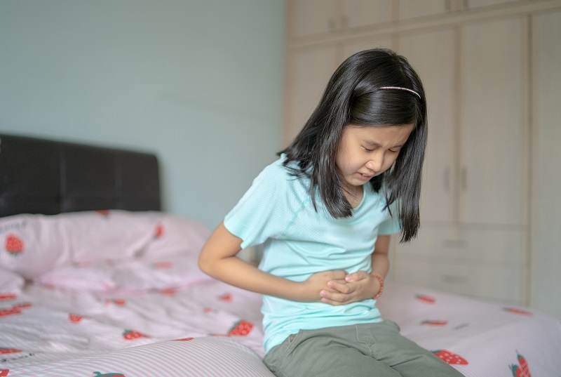 Young girl experiencing a stomach ache. Clenching her belly from digestive issues.