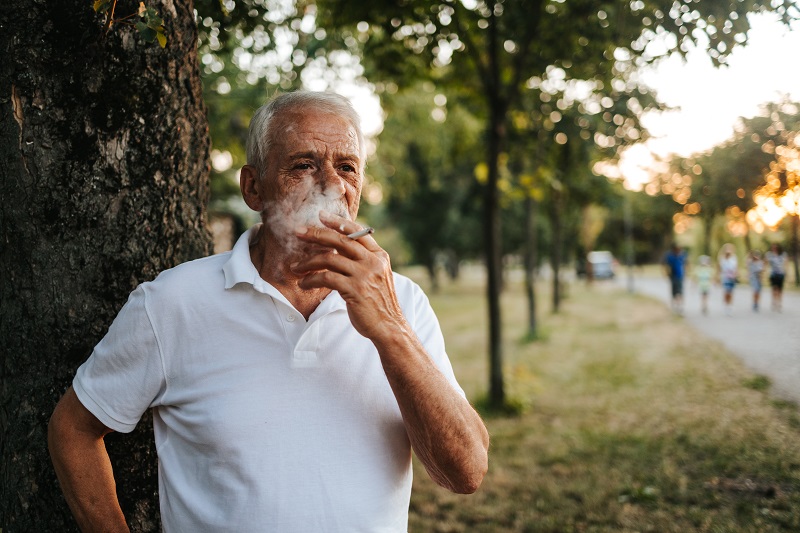 Older man smoking a cigarette outside.