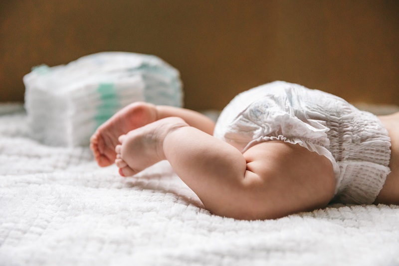 A baby's diaper and legs on a blanket with a pile of diapers in the background. What your baby's poop means.