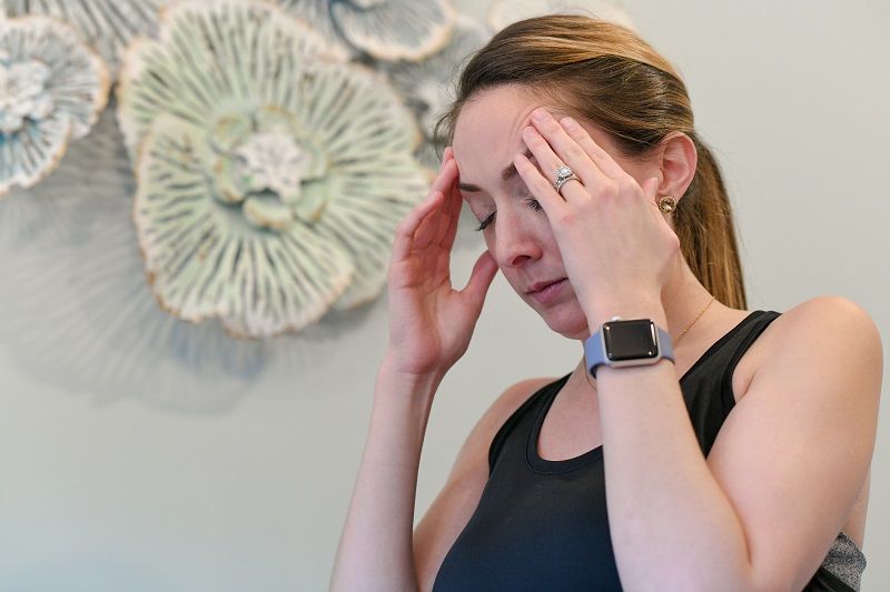 Woman with her hands on her forehead, clenching from a headache or migraine.