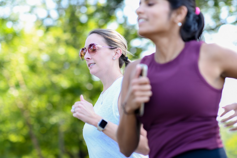 Close up of two young women jogging together outside.