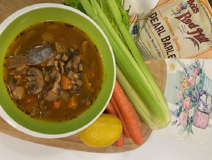 Bowl of mixed mushroom barley soup, with some of the ingredients beside it, including celery, a carrot and a lemon.