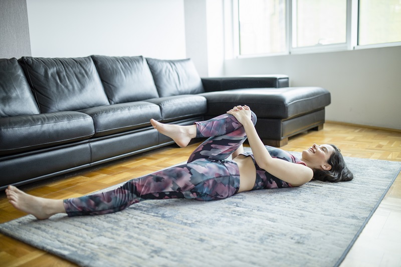woman laying on a mat stretching pulling her knee to her chest, stretching her hip