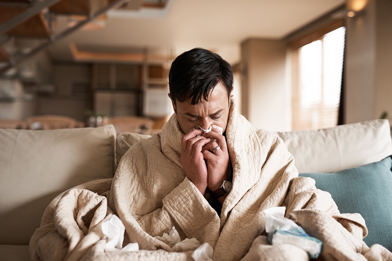 Man at home sick with the flu on the cough blowing his nose with a tissue