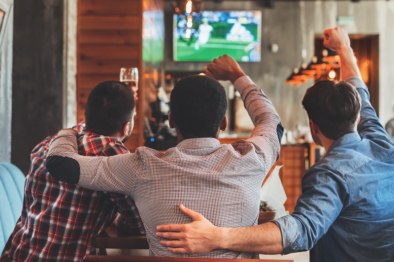 Three men watching football on TV in sport bar, back view