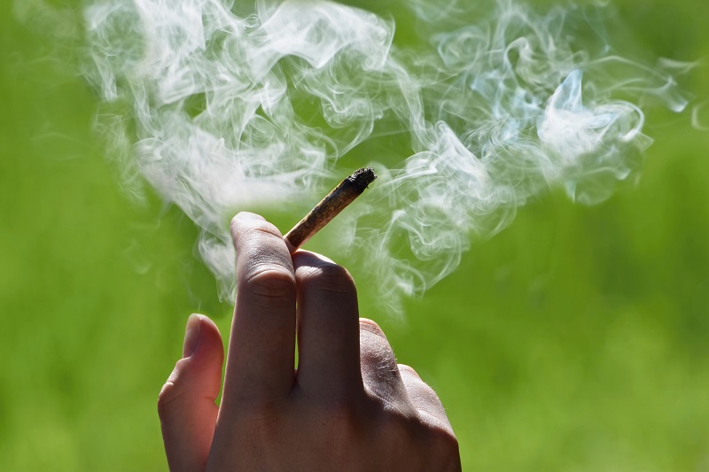 Hand holding a marijuana joint with smoke around it.