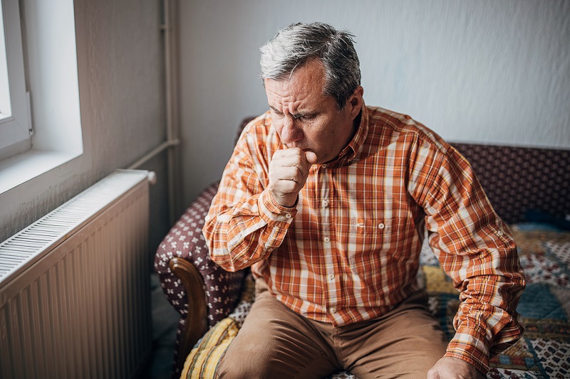 Older man coughing into his hand, managing a lingering cough.