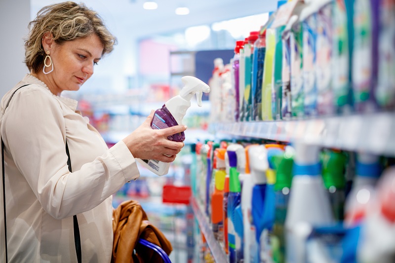 Woman reading the ingredients label on a cleaning spray in the aisle of a grocery store - being mindful of cancer causing ingredients.