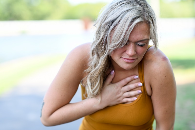 Young woman with blonde hair clutching her chest in pain, suffering from heart burn