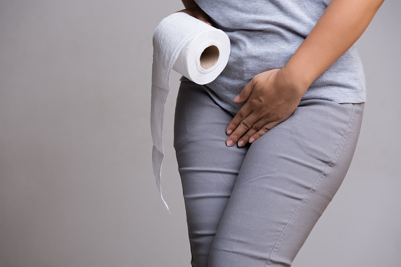 Woman crossing her legs, holding a roll of toilet paper and trying to hold in her urine. Bladder leakage concept. 