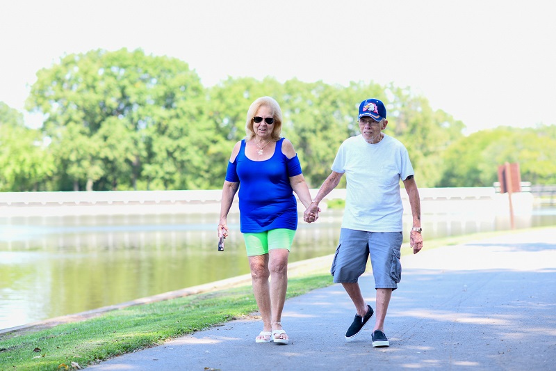 An elderly couple walking through the park together holding hands