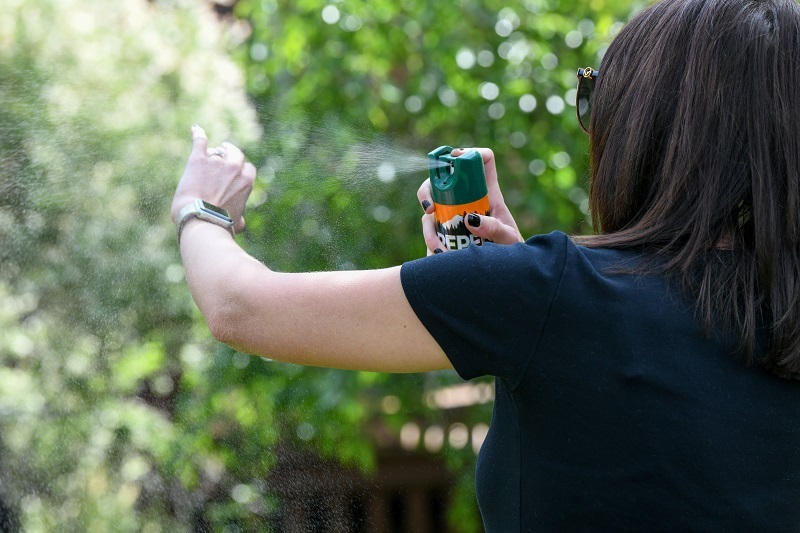 Woman spraying bug spray on her arm while outside.
