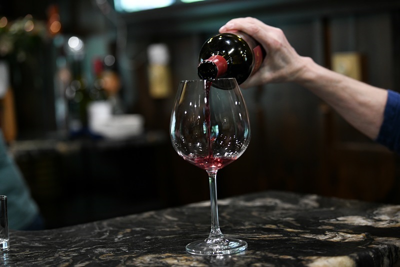 Woman's arm pouring a glass of wine at a bar.