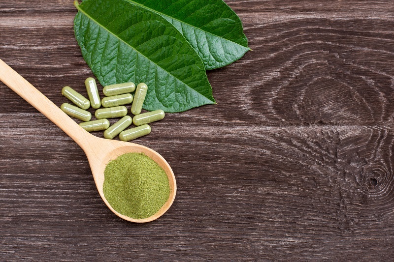 Green Kratom leaf with kratom powder capsule isolated on wooden table background.