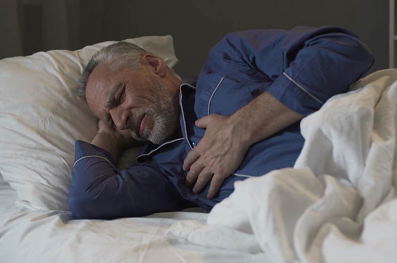 Man sleeping, suffering chest pain while laying in bed, holding his chest.