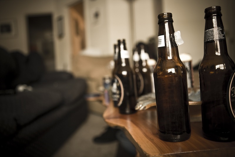 Numerous empty beer bottles on a coffee table. Binge drinking effects.