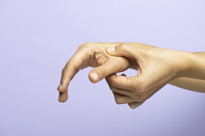 Close up of hands, on a purple background. One hand is putting pressure on the other hand, between the thumb and the index finger. Acupressure for stress relief.
