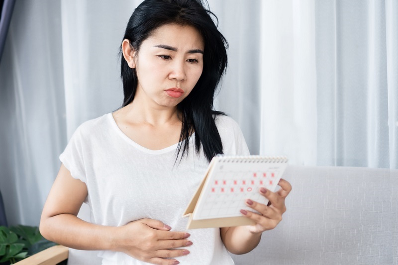 Woman holding a calendar, hand on her stomach, worried about missing her period.