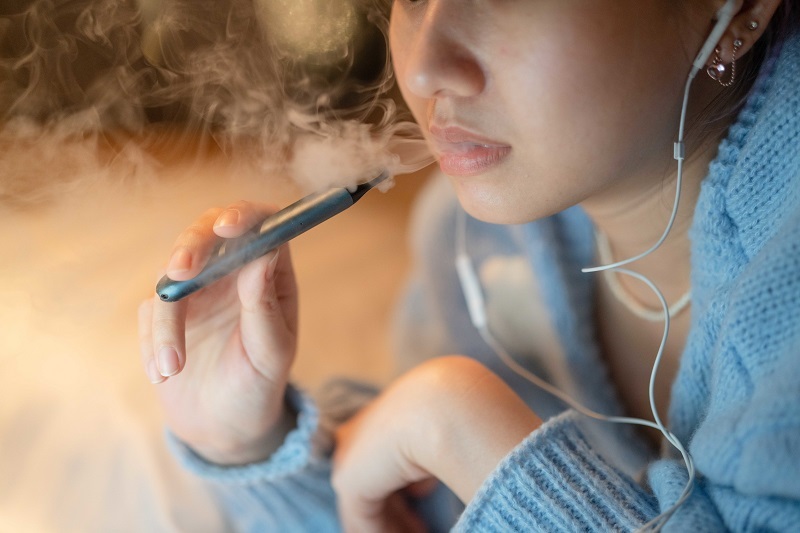 Close up shot of a young woman vaping an electronic cigarette at night