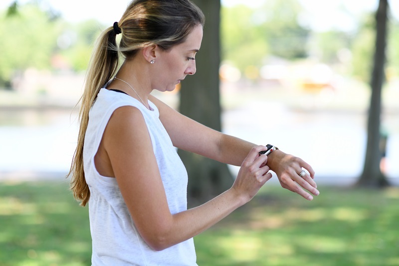 Woman checking her smartwatch while on a run outside on a hot and humid day.