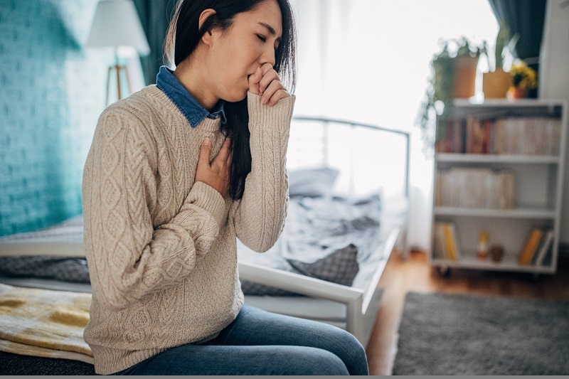 Woman having chest pain and coughing while sitting in her home.