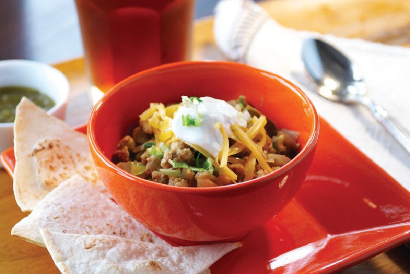 A red bowl of turkey chili topped with sour cream and shredded cheese.