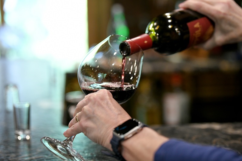 red wine being poured into glass by man wearing a watch
