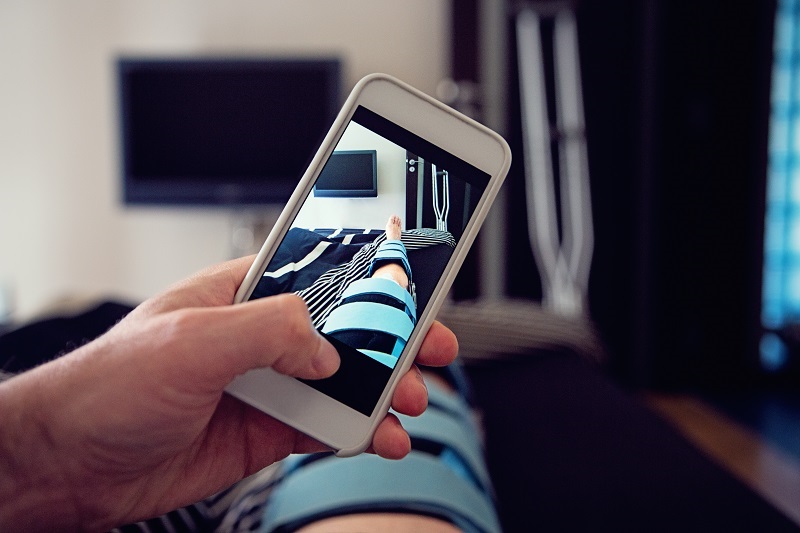  Man laying in bed taking a picture with his phone of his leg in a brace, recovering from ACL tear. 