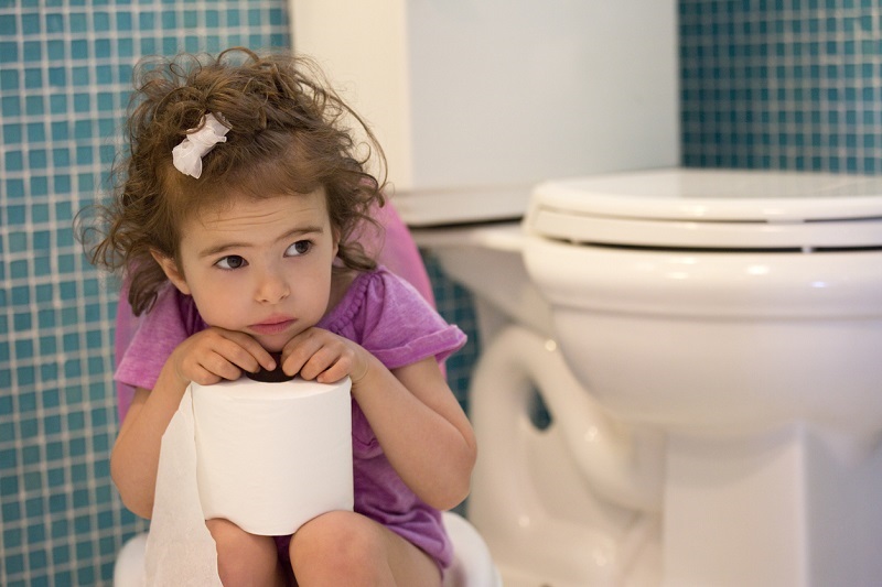 Little girl sitting on the potty in the bathroom, holding a roll of toilet paper.