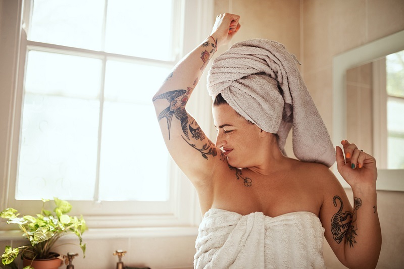 Woman in a towel, smelling her armpit, observing body odor.