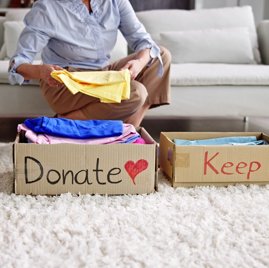 Woman decluttering her home and organizing clothes into boxes, one labeled "donating" and the other "keep". 