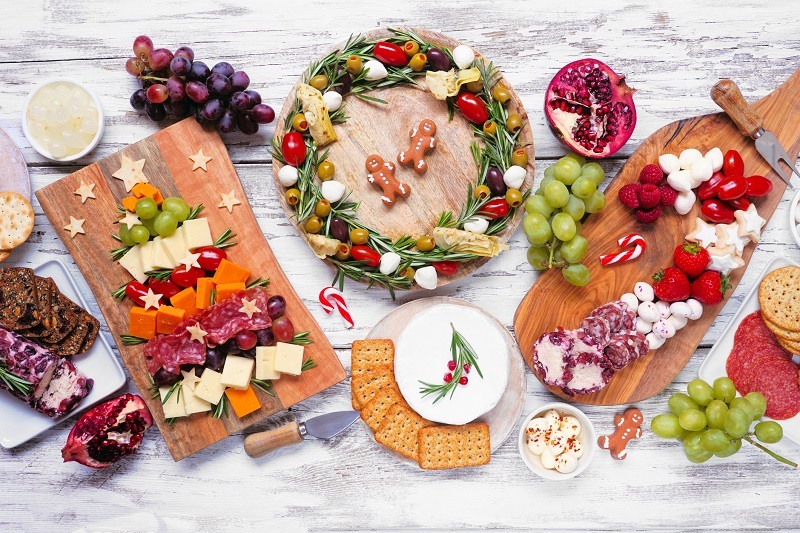 Christmas charcuterie table scene over a white wood background. Selection of cheese and meat appetizers. Christmas tree, wreath and candy cane arrangements.