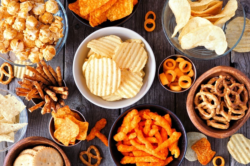 An assortment of chips and processed snacks in bowls on a table. 