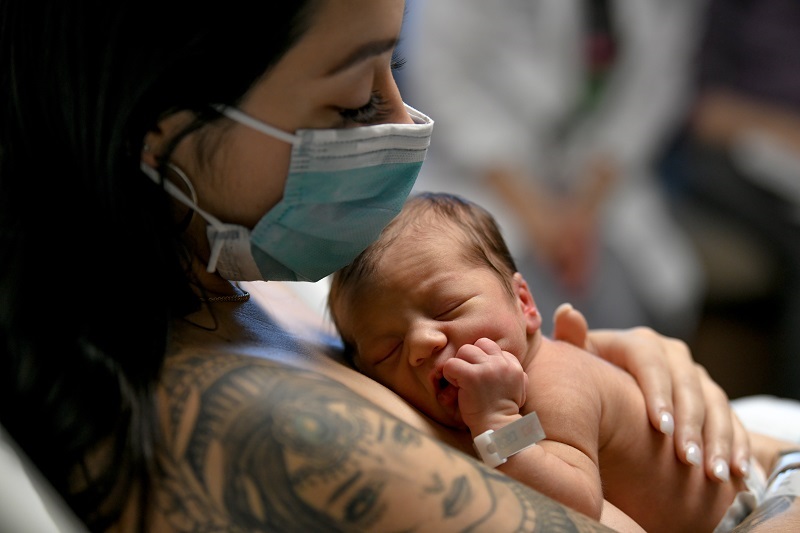 Mom holds newborn baby to chest for skin to skin contact. Image concept for c-section recovery.