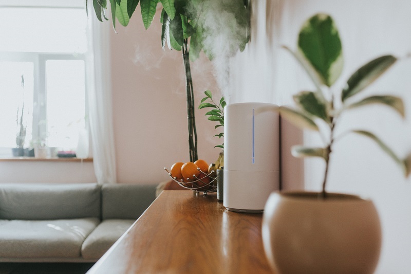 A humidifier releasing steam on a counter space in a living room. 