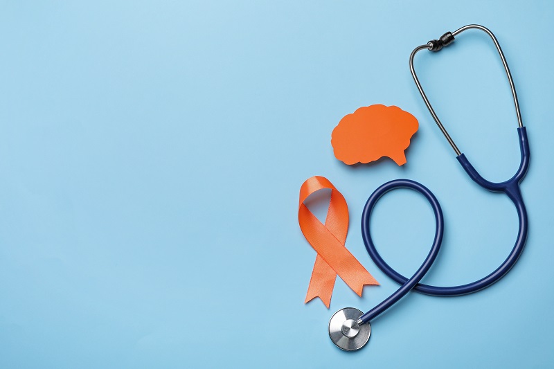 Orange ribbon, stethoscope and paper brain cutout on light blue